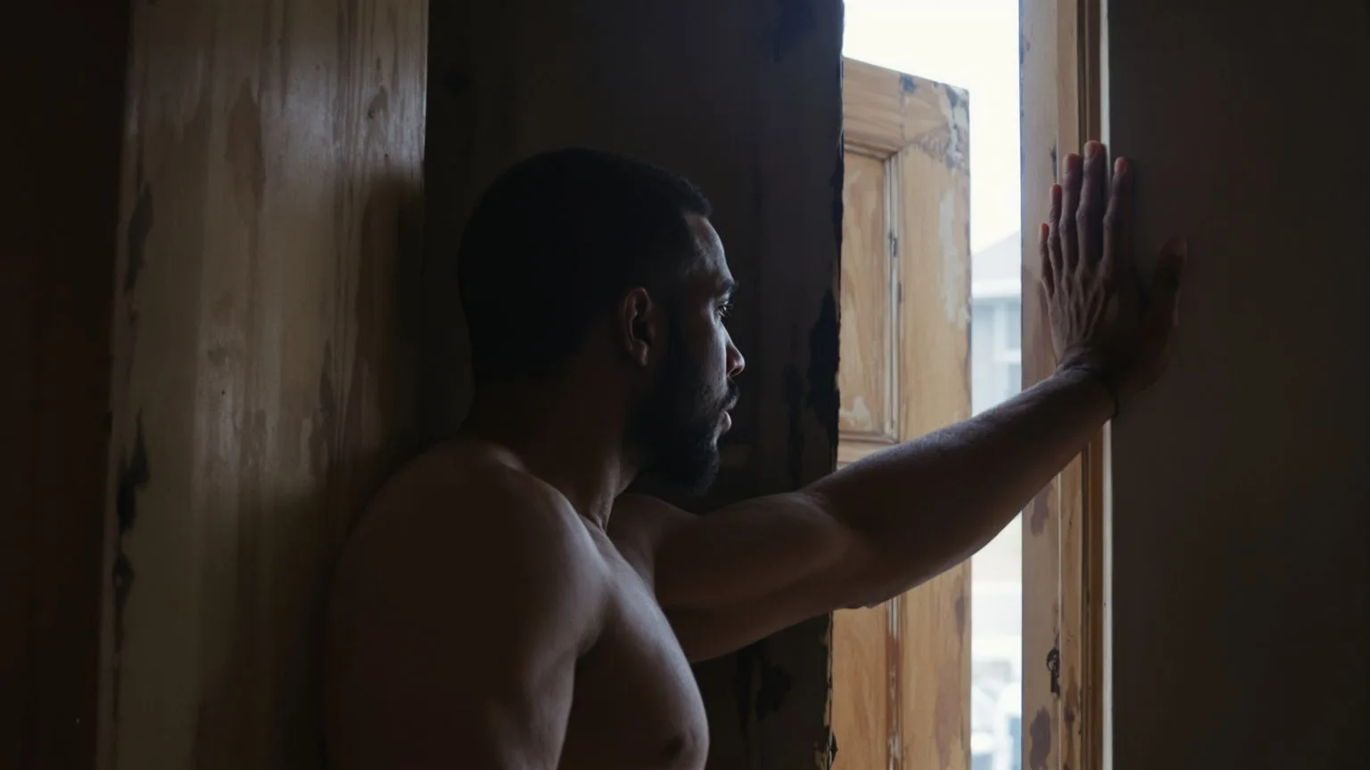 Man leaning against doorframe between dark interior and daylight during dark night of the soul