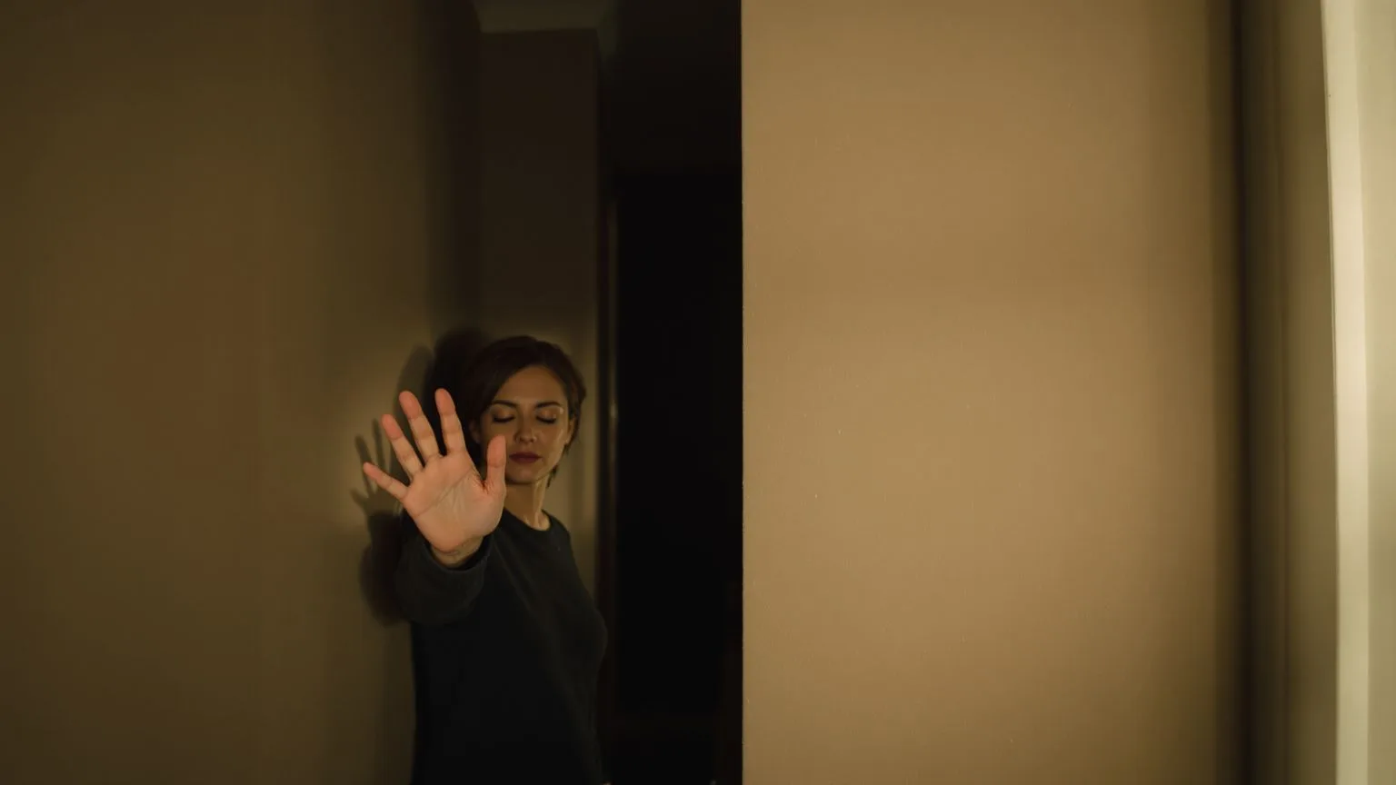 Woman pressing hand against hallway wall with eyes closed feeling tension in the body