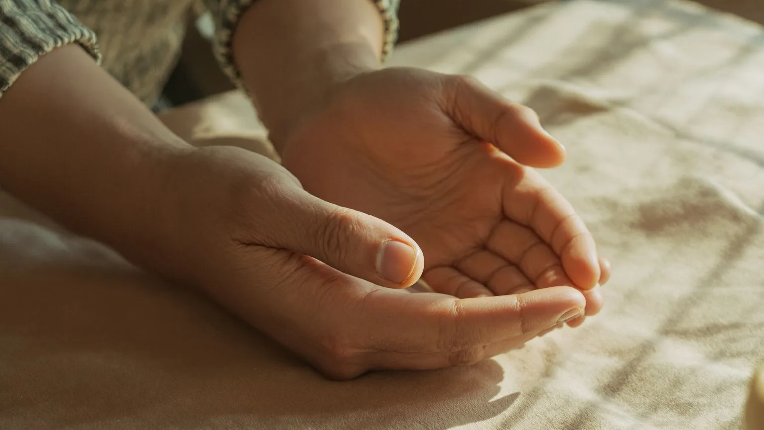 Close-up of hands resting on linen showing the body releasing tension and finding stillness Close-up of hands resting on linen showing the body releasing tension and finding stillness