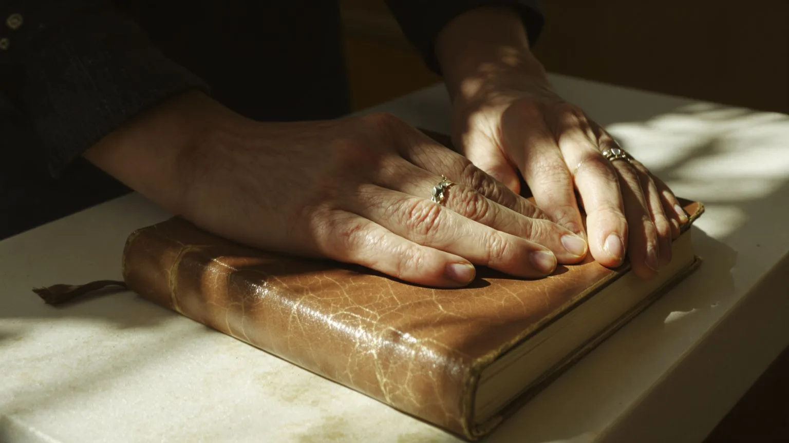 Hands releasing grip on a journal as the body softens from urgency into stillness