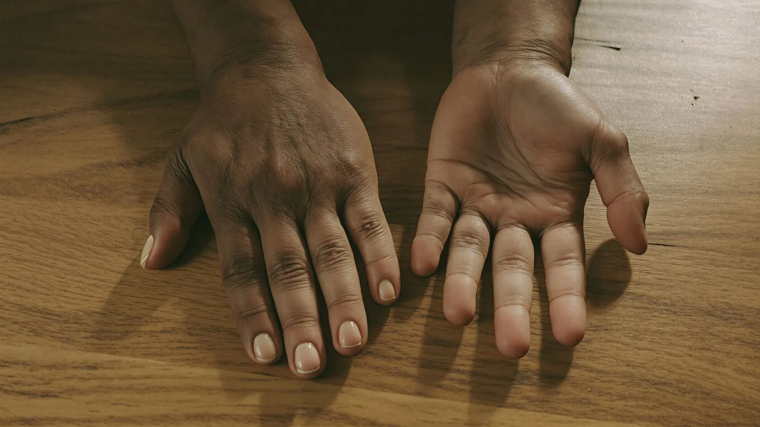 Close-up of hands uncurling on wooden table in natural light showing body releasing freeze response