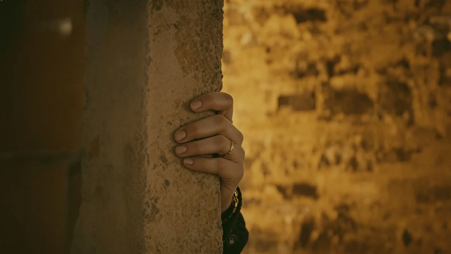 Hands gripping stone doorframe at threshold between shadow and light representing freeze response in spiritual practice