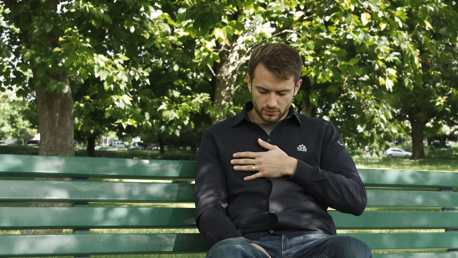 Man on a park bench with hand on chest reading body signals using somatic grounding techniques