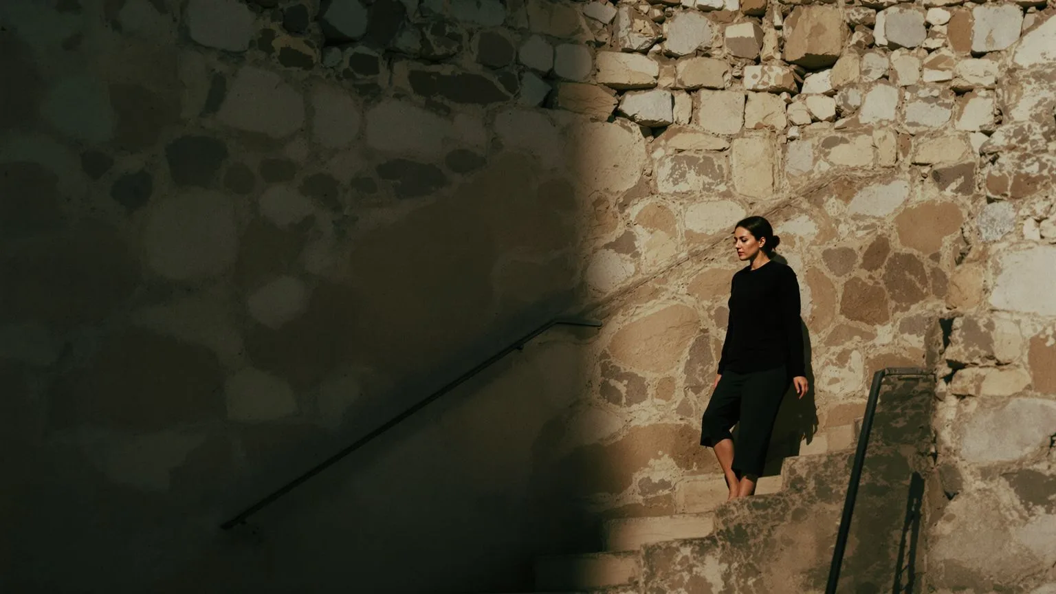 Woman paused on stone steps between shadow and light illustrating why understanding triggers doesn't calm the body