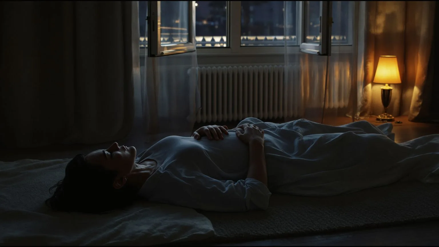 Person lying on a rug at night with hand on stomach, body finally settling as nervous system activat Person lying on a rug at night with hand on stomach, body finally settling as nervous system activation eases