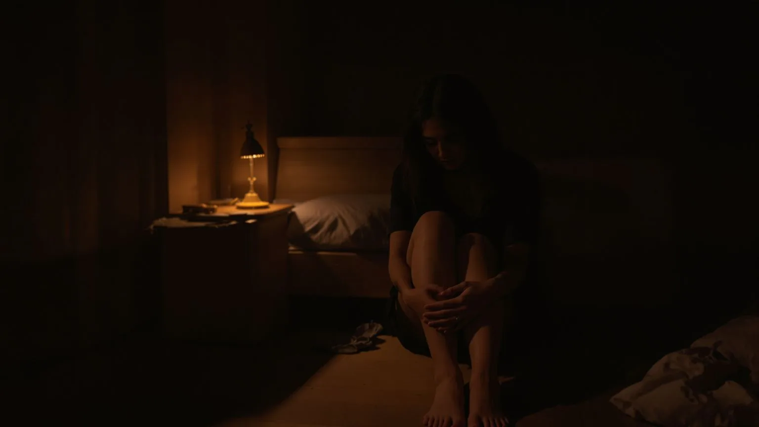 Woman seated on floor beside bed at night beginning a 12-minute self compassion reset