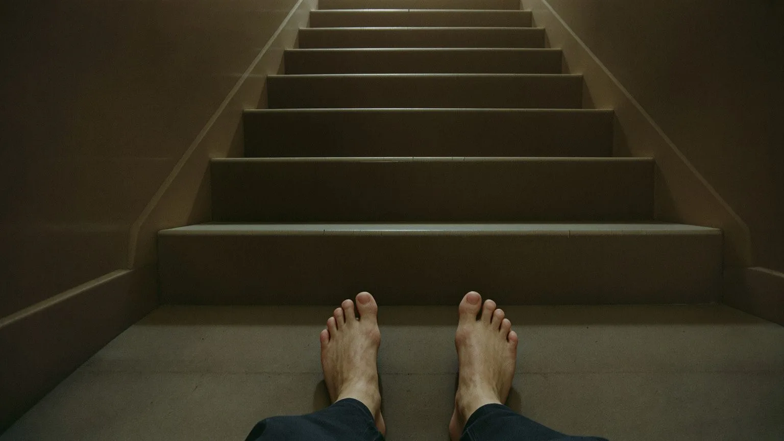 Bare feet paused at bottom of concrete staircase in natural light showing hesitant first step toward support