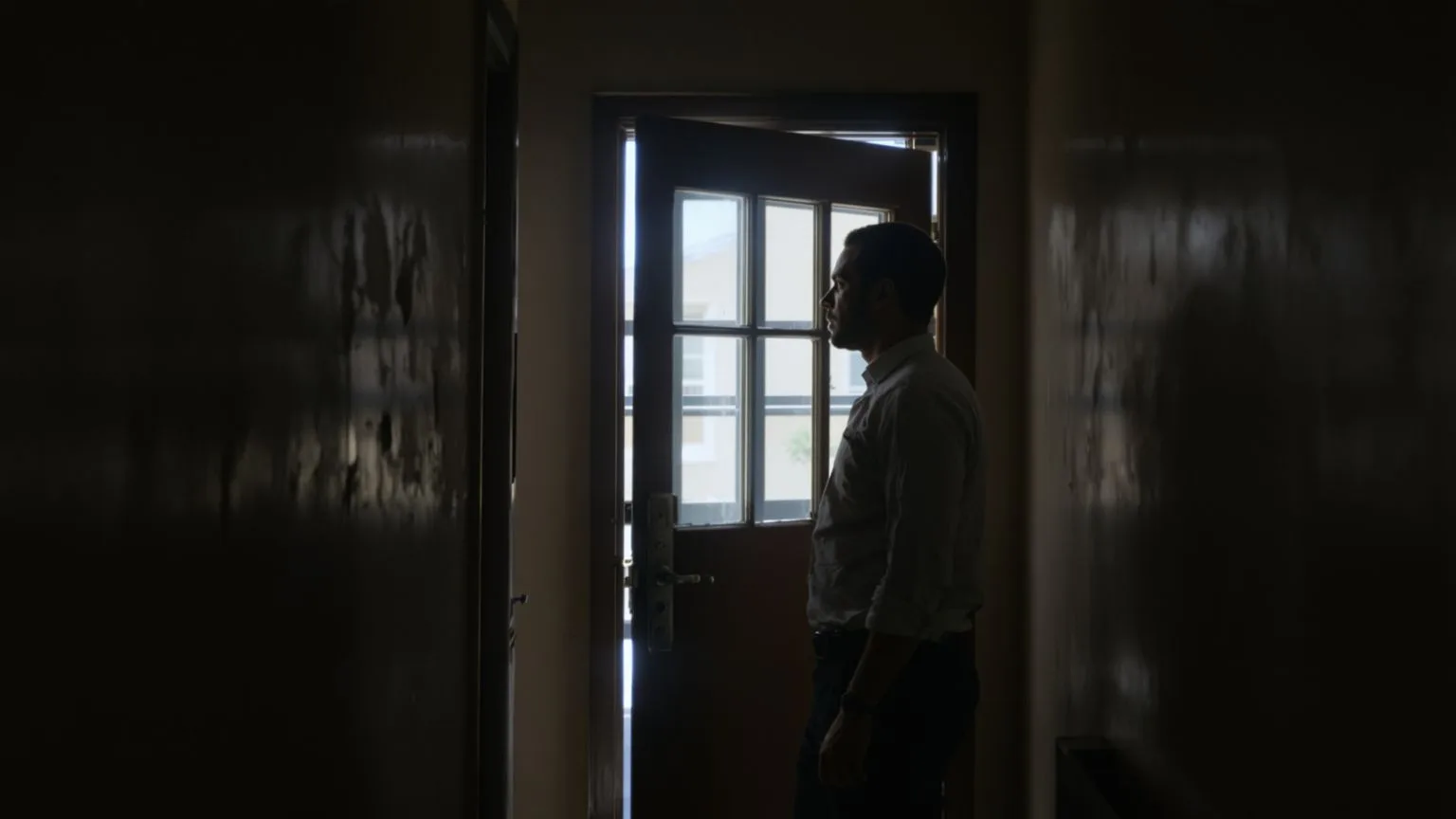 Man hesitating at doorway threshold with hand near chest showing the invisible wall the body notices first