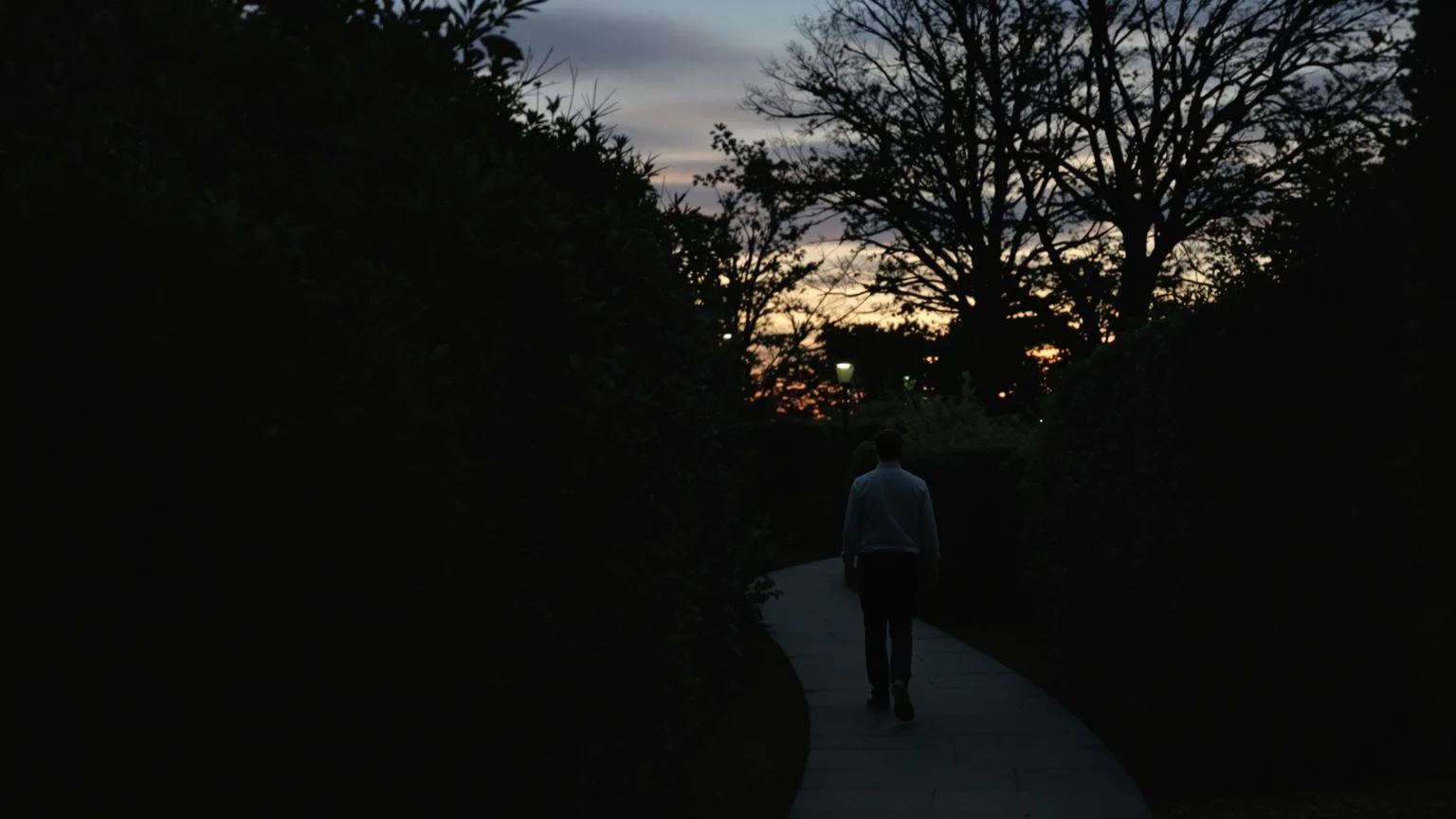 Person walking stone garden path at twilight afraid to show real feelings but moving forward