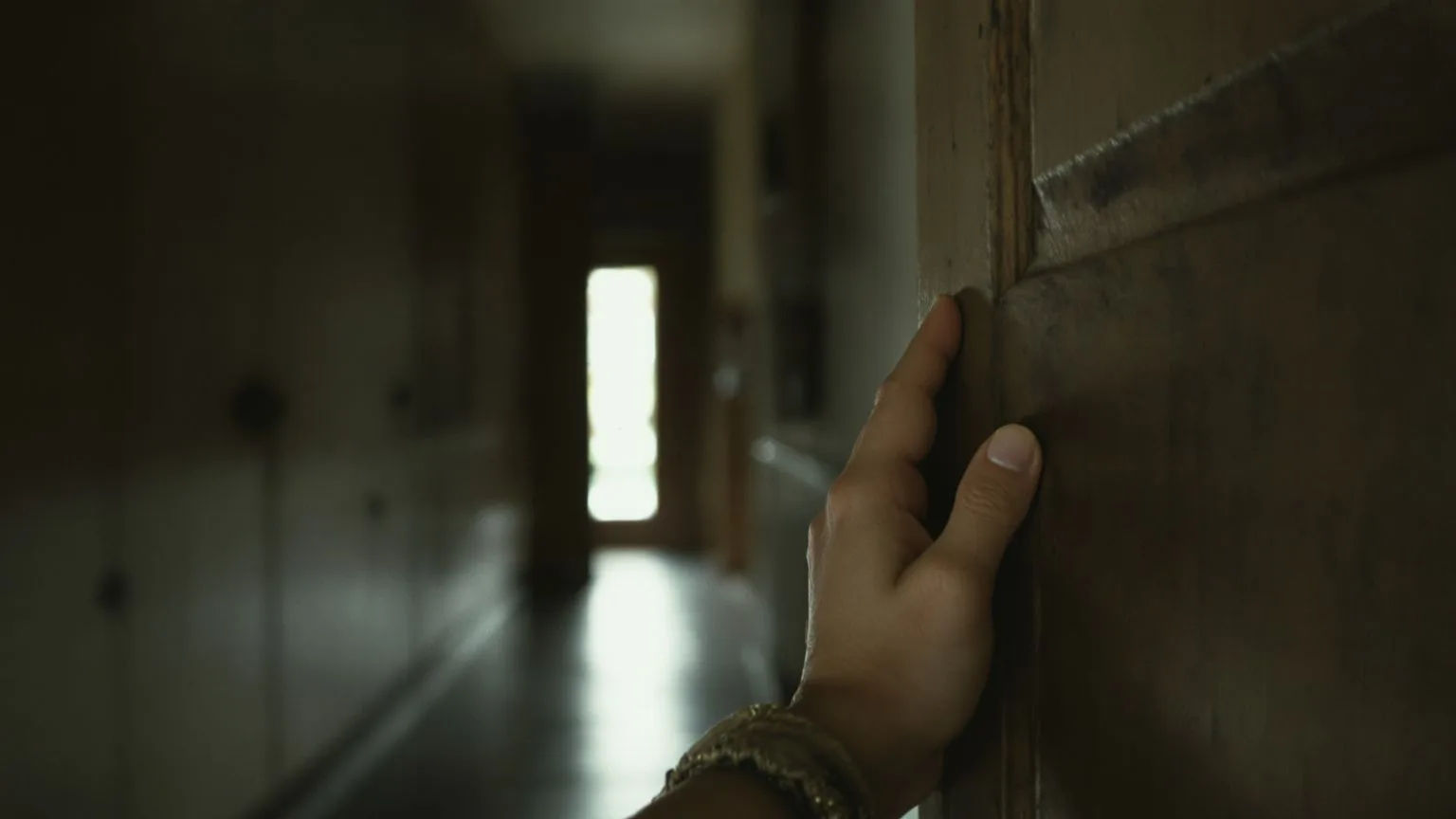 Hand gripping a wooden doorframe at a threshold between shadow and light, testing trust in small steps
