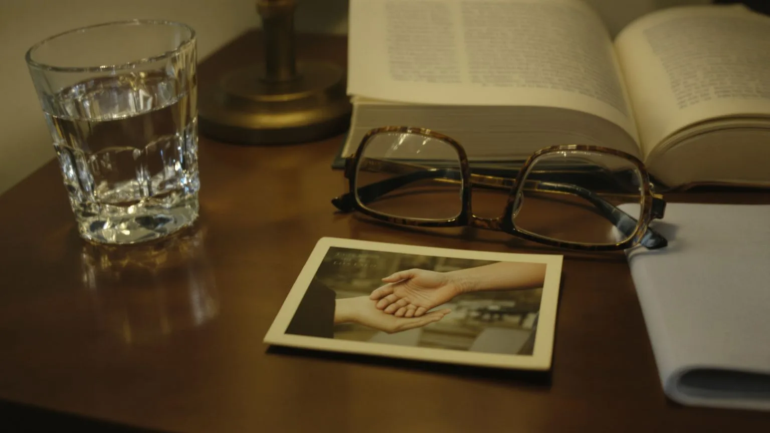 Old childhood photograph beneath everyday objects on nightstand revealing childhood wounds in adult life