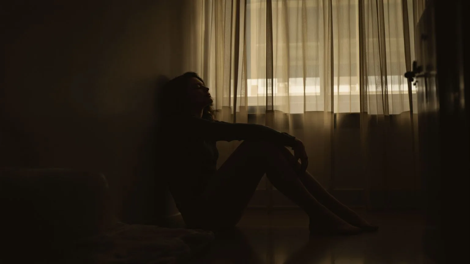 Person sitting quietly on wooden floor in dim bedroom, finding stillness when feeling spiritually lost