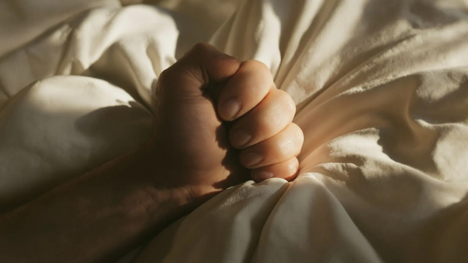 Man's hand releasing a fist on linen sheet showing why surrender feels impossible when needed most