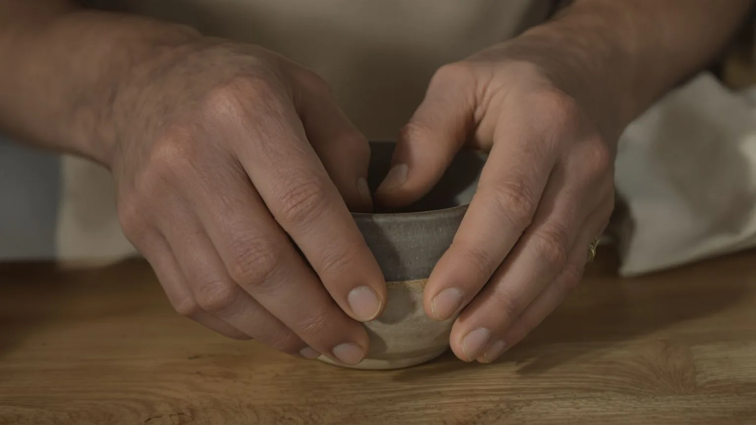 Hands resting on a ceramic bowl on a wooden table showing the body loop of relationship anxiety