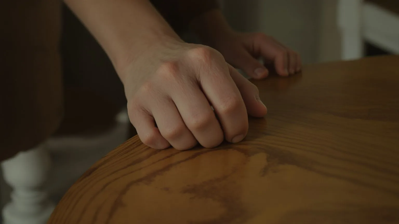 Close-up of tense hands gripping wooden table edge showing how walking on eggshells gets wired into the body