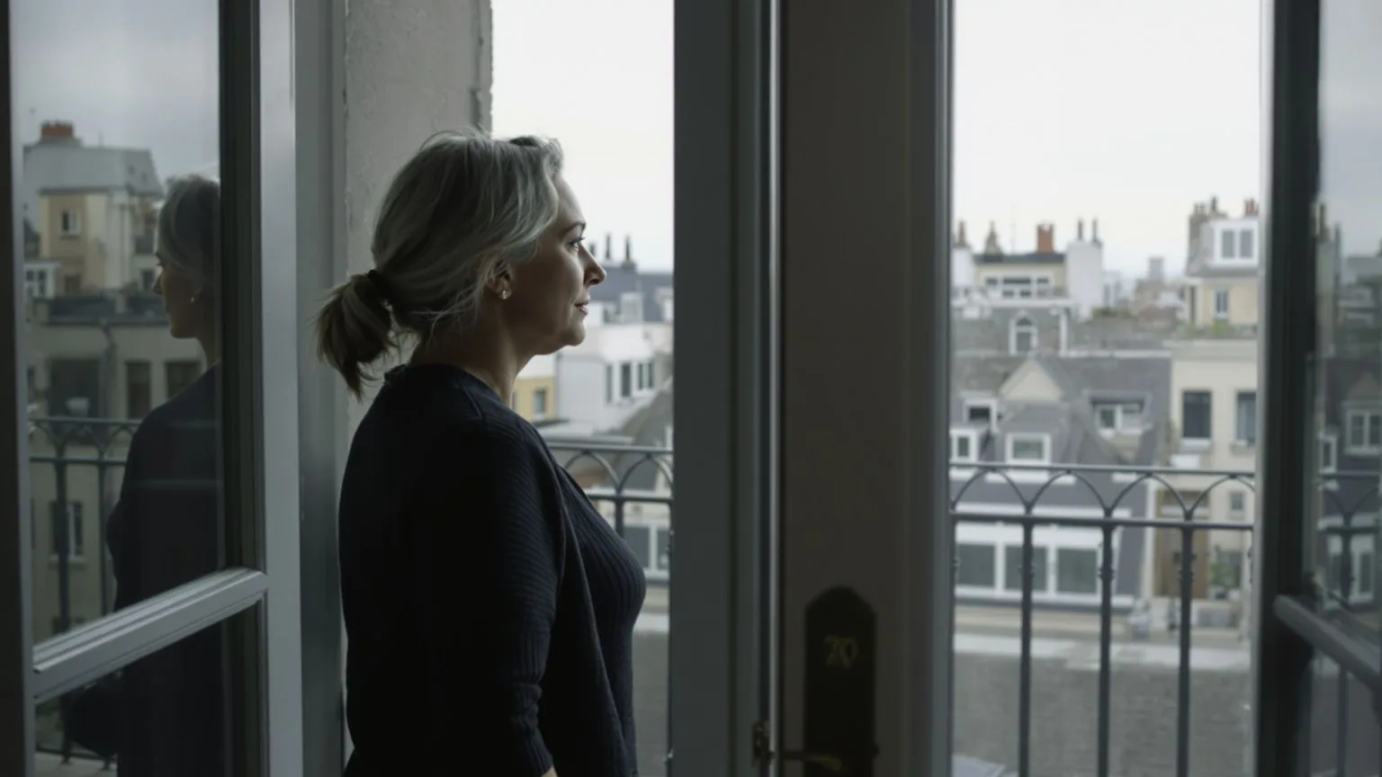 Woman standing at open balcony doors looking outward with soft light on her face, how you got here