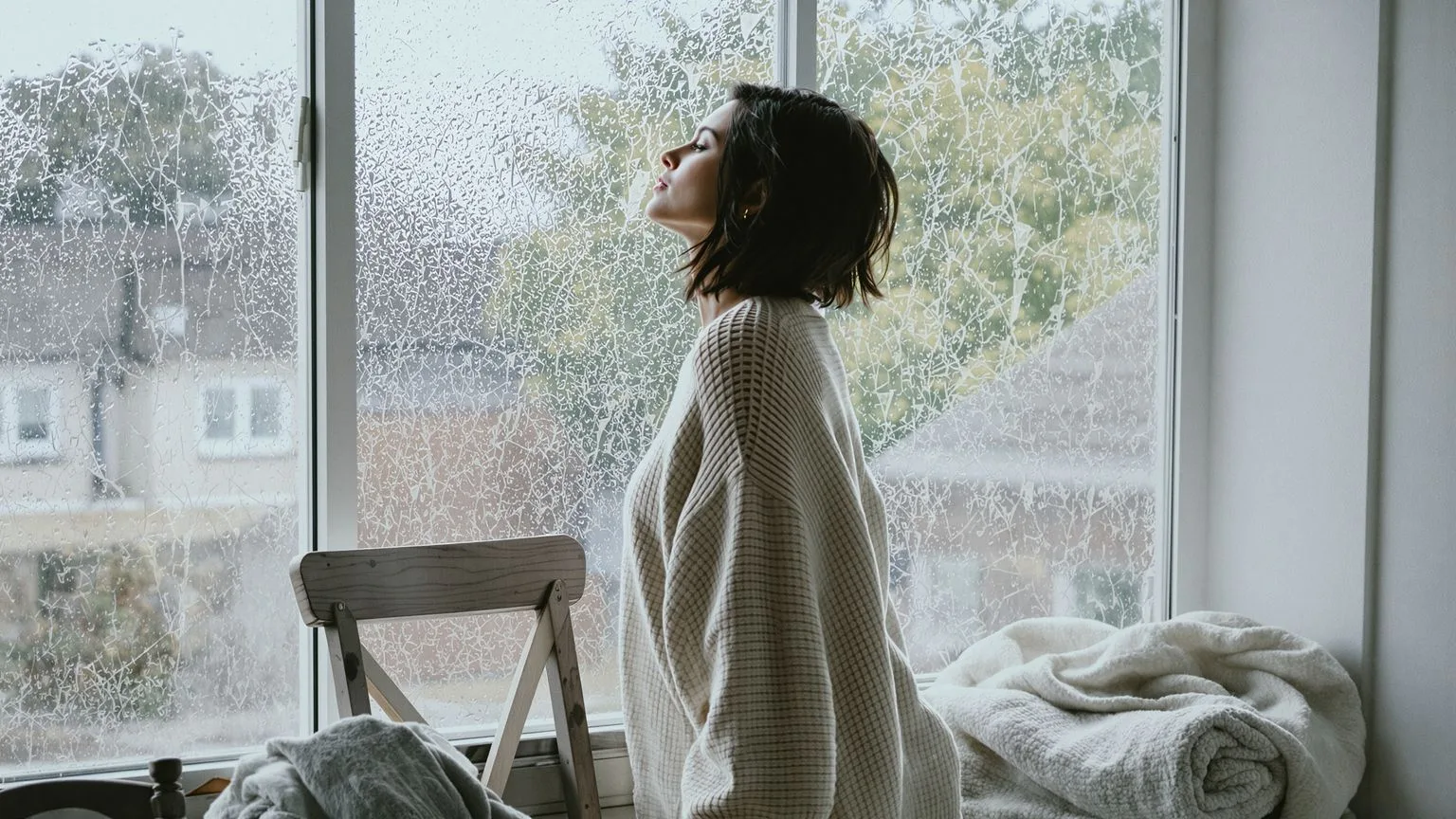Woman silhouetted behind rain-streaked window pane representing stages of grief breakup