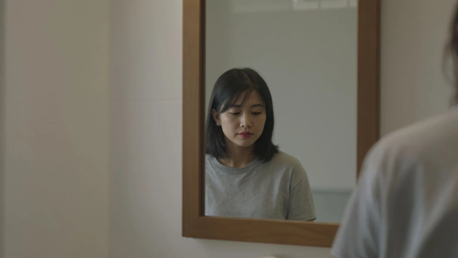 Woman's reflection in bathroom mirror showing what people pleasing actually costs you in quiet erosion