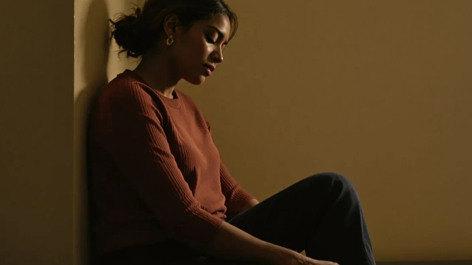 Woman sitting on a low wooden bench, eyes closed, embodying emotional language through quiet inward stillness in warm diffused light