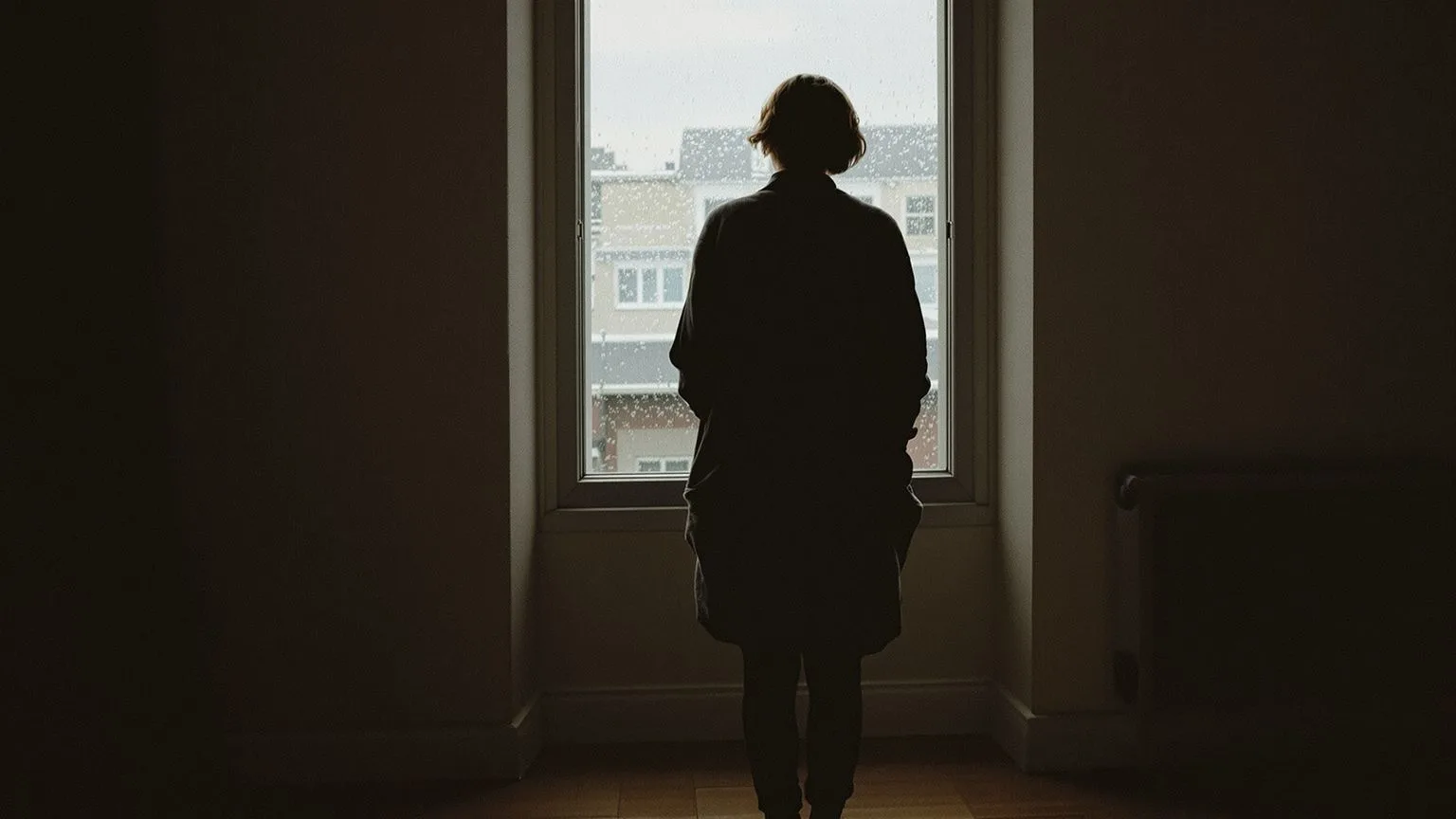 Person at window experiencing multiple anxiety symptoms including chest tightness