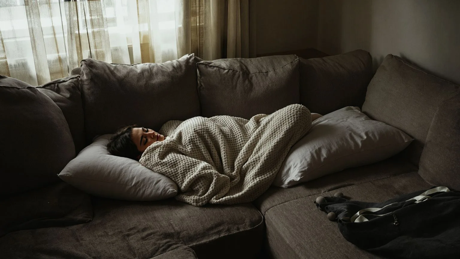 Woman resting on a dim sofa with eyes closed, living with chest tightness anxiety in quiet afternoon stillness