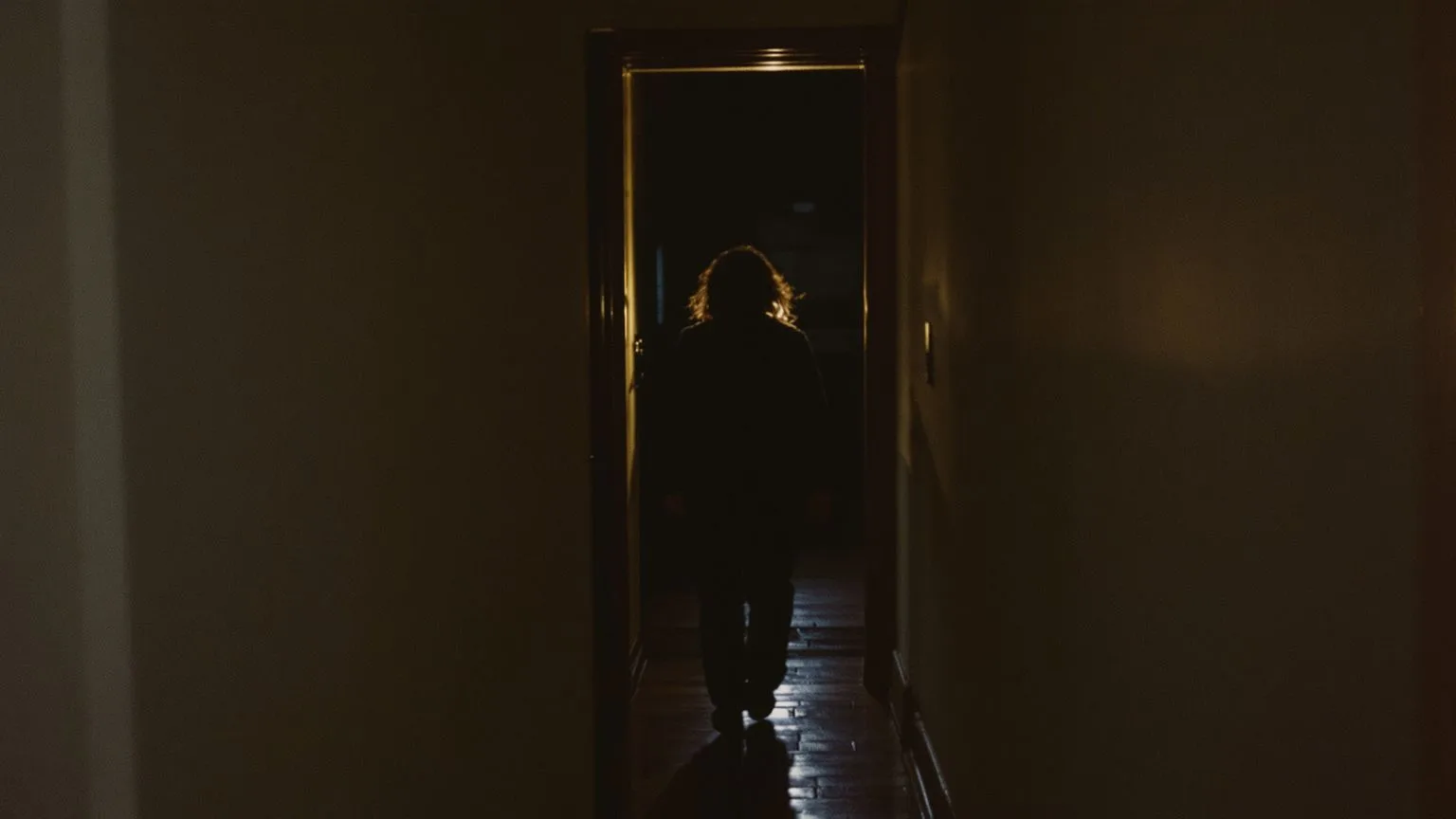 Person walking through dark hallway at night representing why racing thoughts get worse in darkness