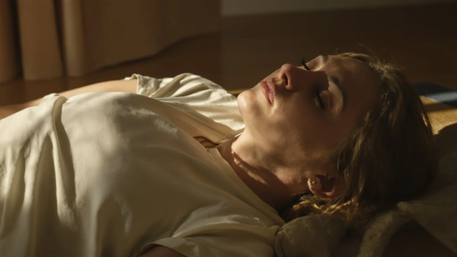 Woman in Feeling Session posture on a grounded mat, T-shirt over eyes, side angle, embodying a phase Woman in Feeling Session posture on a grounded mat, T-shirt over eyes, side angle, embodying a phase of the five-phase process for childhood trauma symptoms